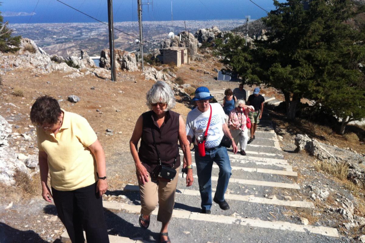 A group of visitors climbing steps at Juktas Peak Sanctuary with the coast in the background