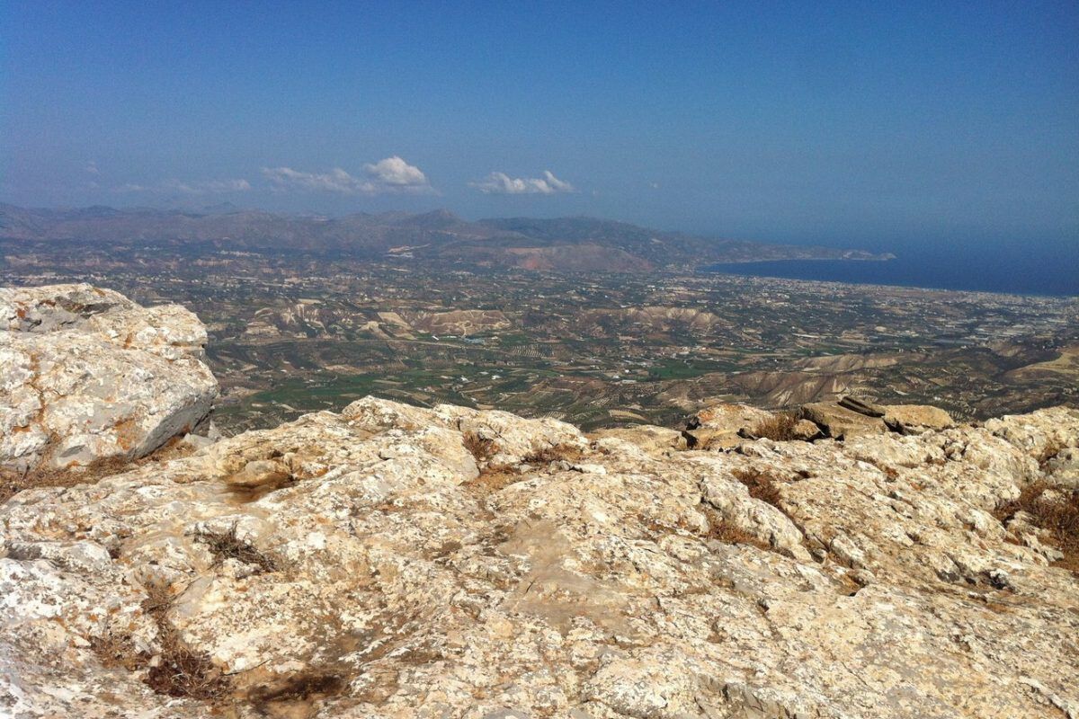 A rocky lookout at the Peak Juktas Sanctuary, overlooking a broad valley and distant coast.