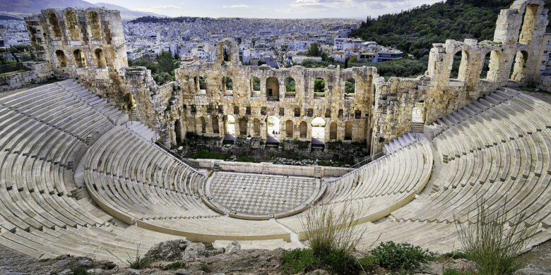 The Odeon of Herodes Atticus, an ancient Greek stone theater with semicircular seating and a grand arched facade, set against the backdrop of modern Athens.