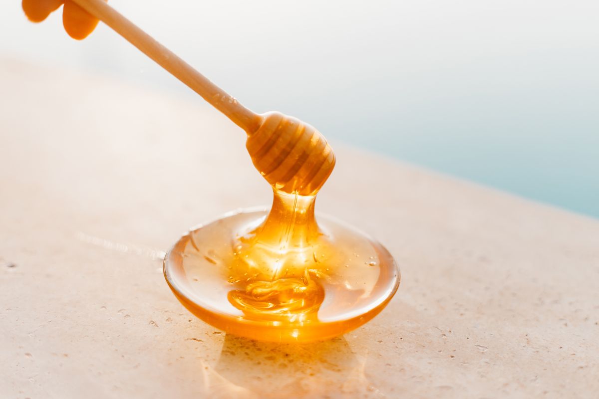 Golden honey drizzling from a wooden dipper onto a glass plate, with a soft, blurred background.