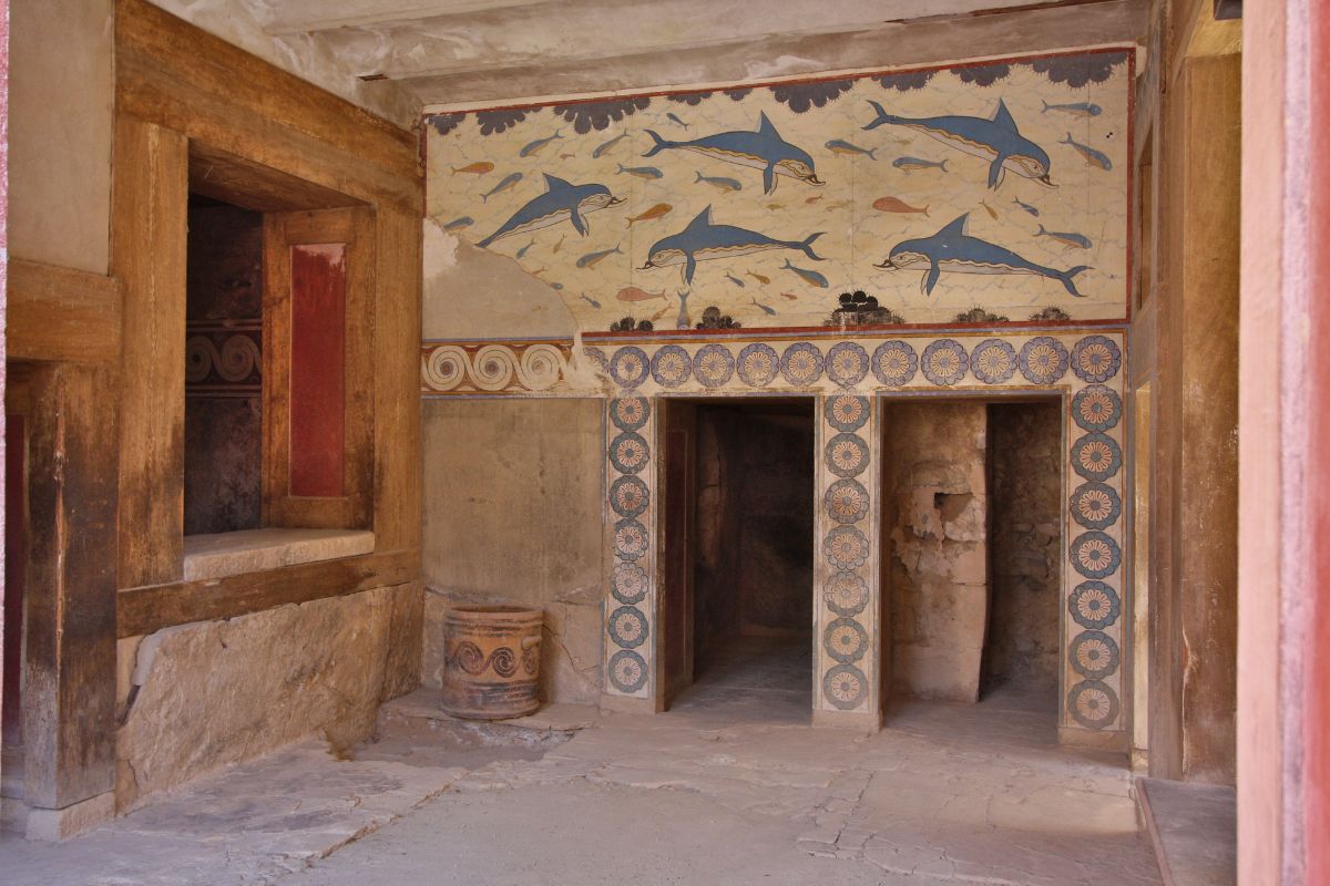 A room inside Knossos Palace featuring a fresco of dolphins on the wall, decorative patterns, and wooden and stone architectural elements.