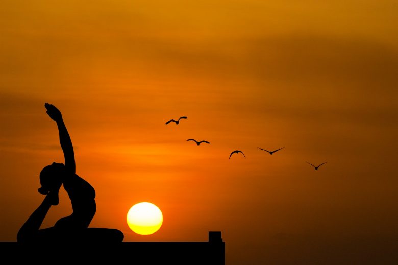 yoga during sunset with birds in the orange sky