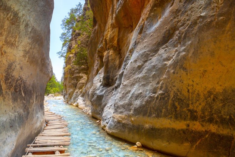 A wooden walkway running through a narrow gorge with a clear stream and steep rock walls.