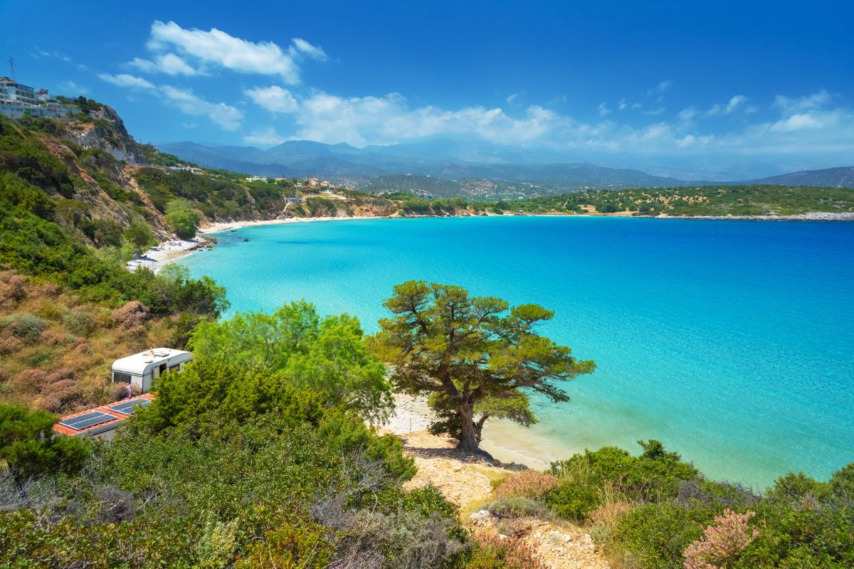 A picturesque view of Voulisma Beach in Crete, featuring turquoise waters, sandy shores, and lush greenery with hills in the background.